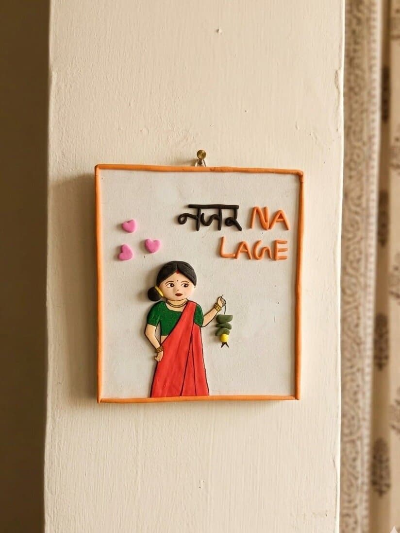 Nazar Na Lage: a small plaque of a woman in a red saree holding nimbu-mirchi, with the words Nazar Na Lage, on a door frame